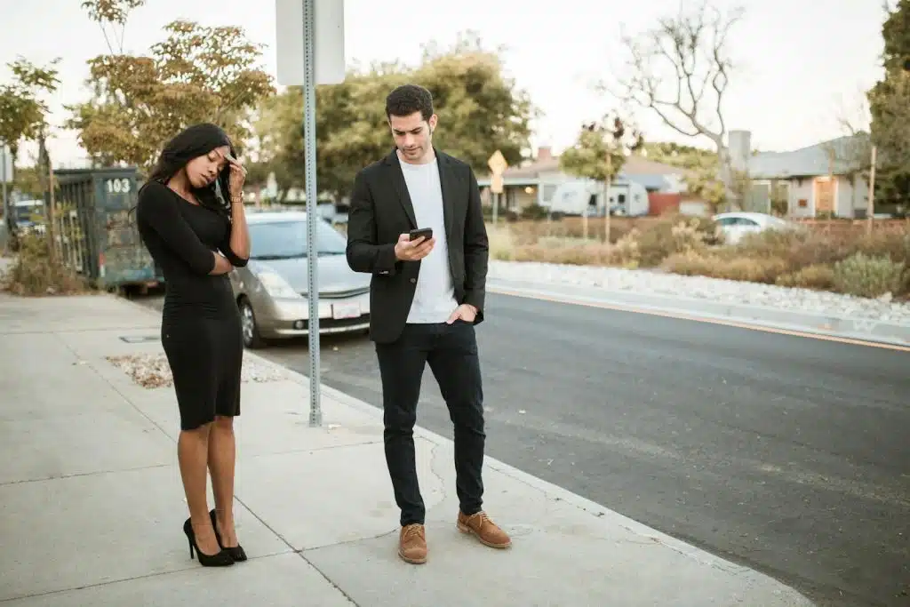 The man is ignoring her woman while standing on the sidewalk.
