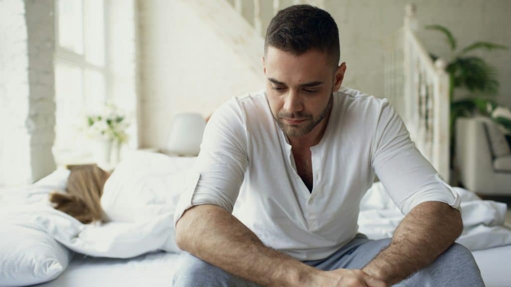 The man is sitting on the edge of the bed while the woman has her back on his.