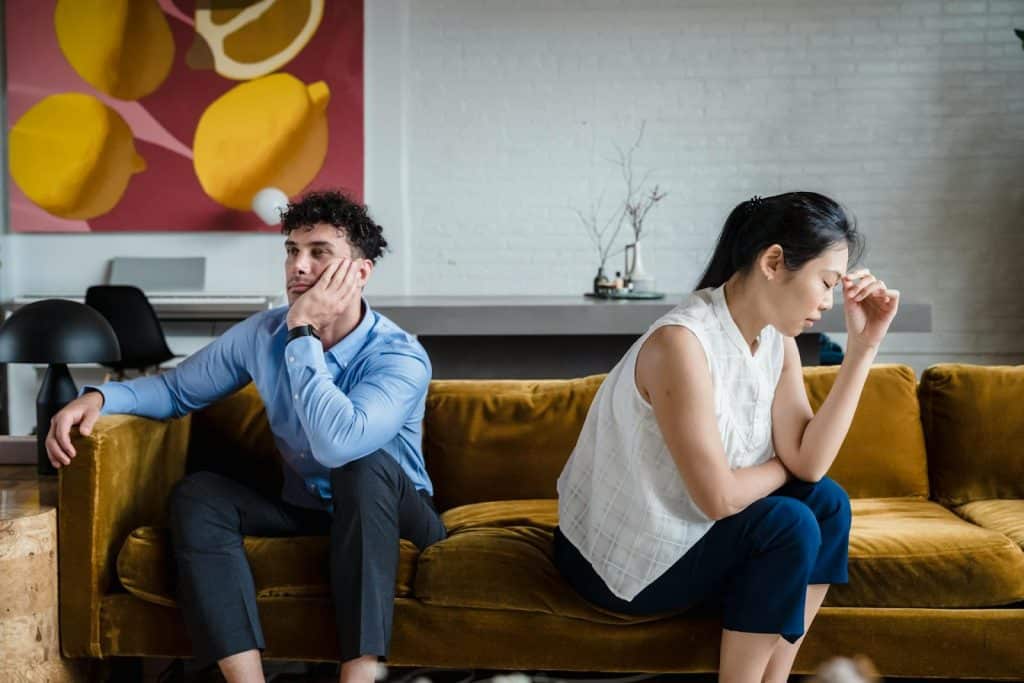 The frustrated woman turns her back on the man while sitting on the couch.