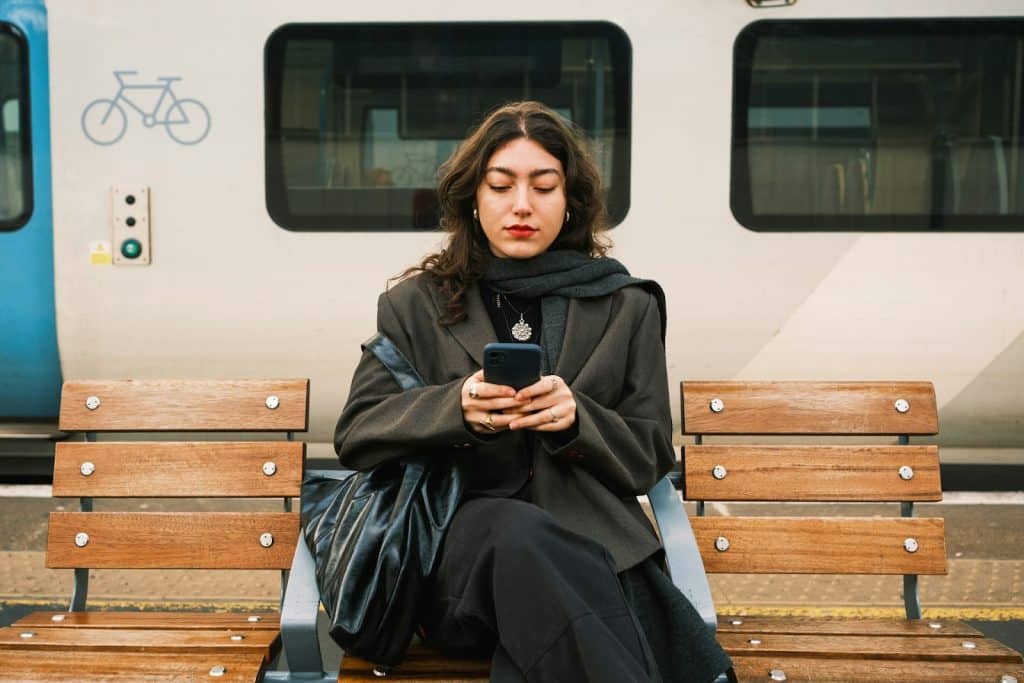 The woman is texting while sitting on a bench.