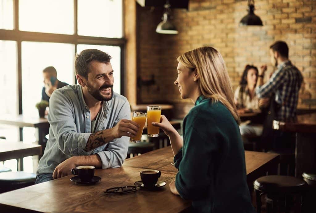 The man and woman are clinking their glasses in a café.