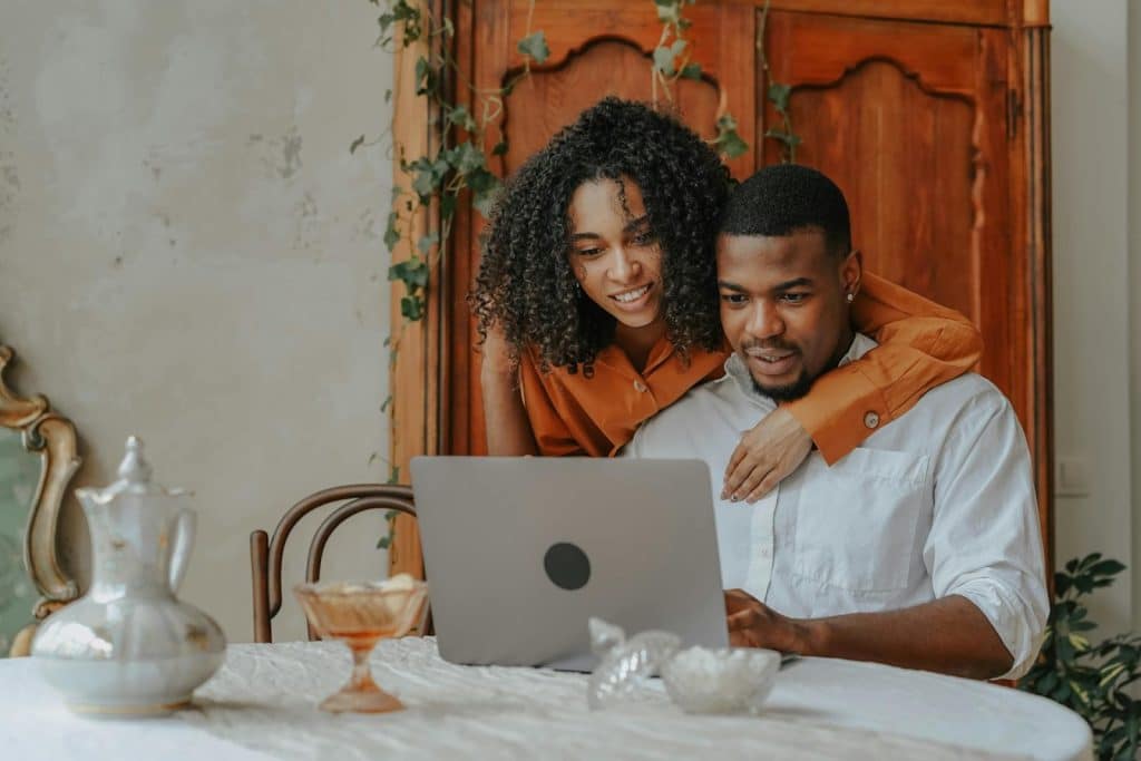 The couple is sitting at the table while looking at a laptop.