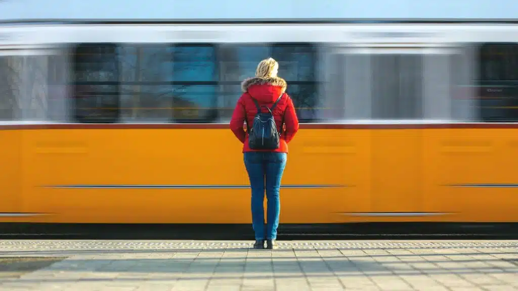 The back view of a woman with a backpack standing still as a fast-moving train speeds by.