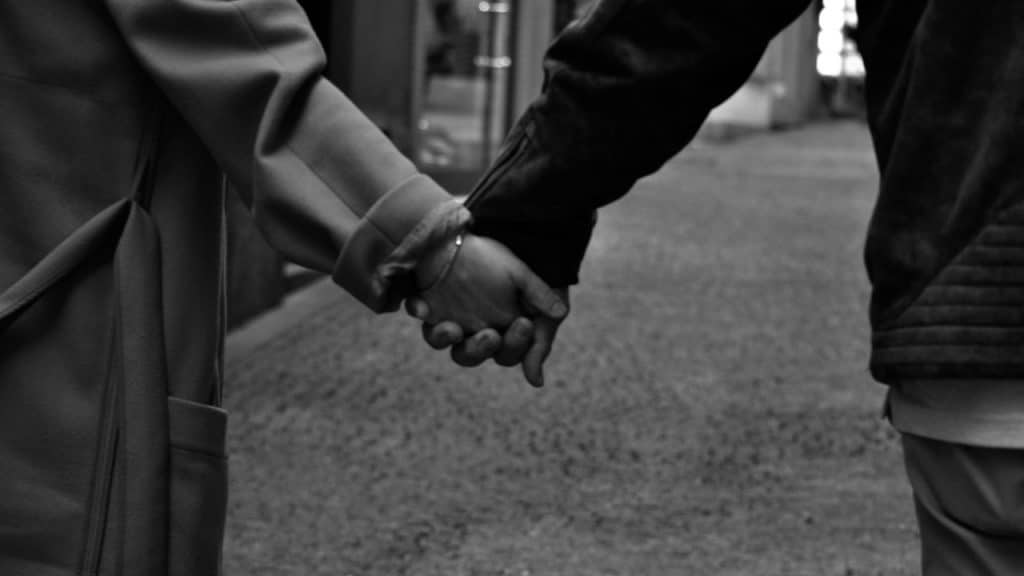 A close-up shot of a couple holding hands while walking down a cobblestone street.