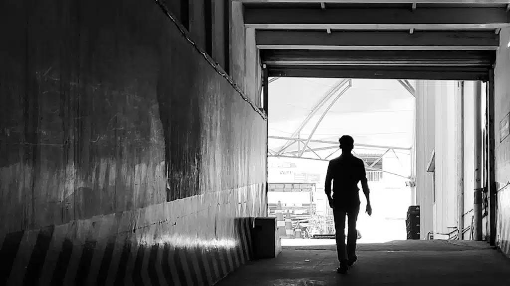 A person walking away from the camera and toward the bright light at the end of a hallway.
