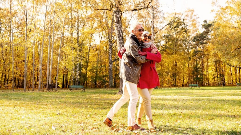 An old couple laughing and hugging in a park.
