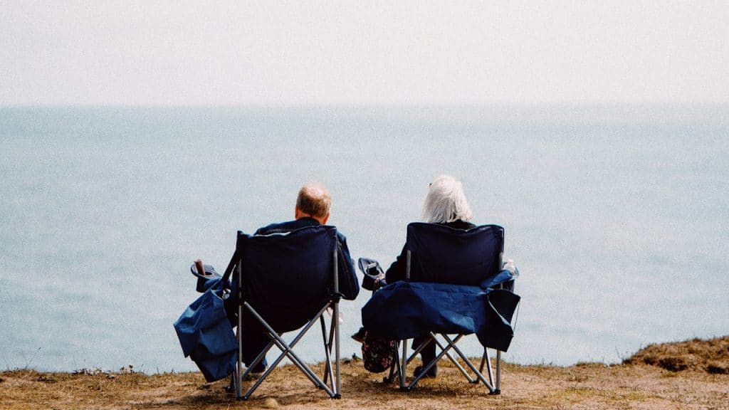 An older couple sitting on chairs on a cliff overlooking the seaside.
