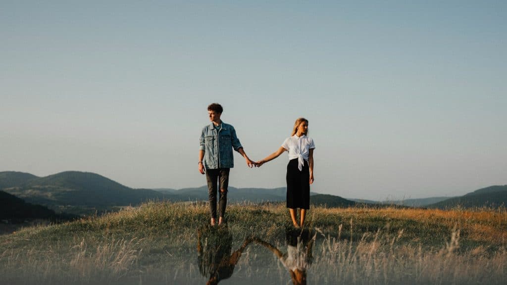 A young couple holding hands on a grassy hilltop at sunset.
