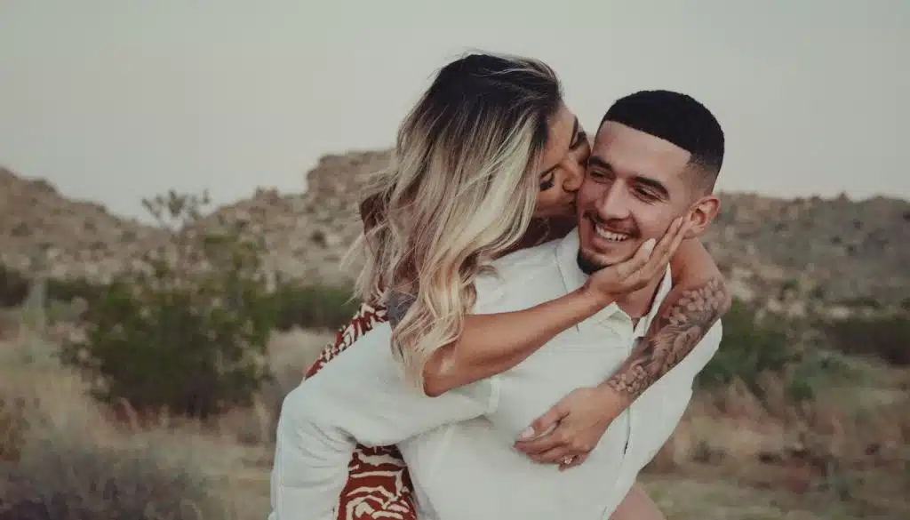 The woman is kissing the man while spending time outdoors.