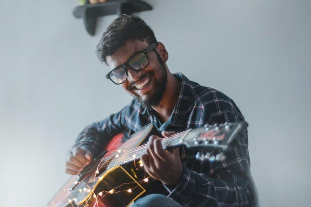 The man is smiling while playing a guitar.