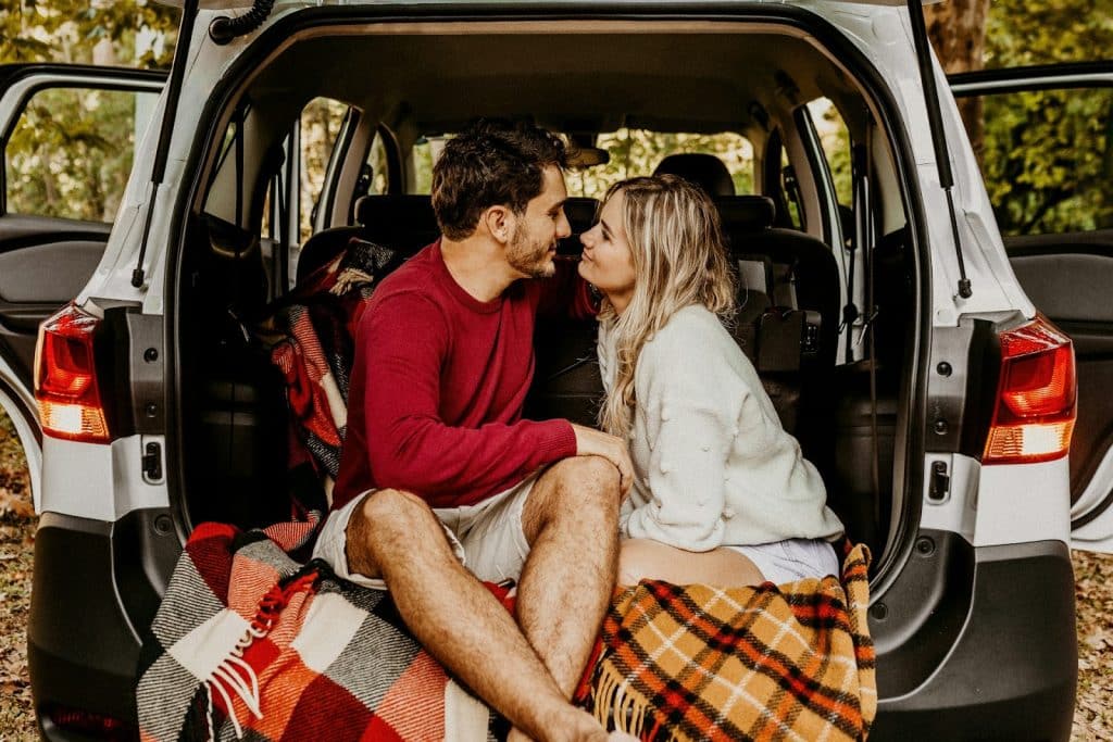 The couple is hanging out in the car’s trunk while looking at each other.