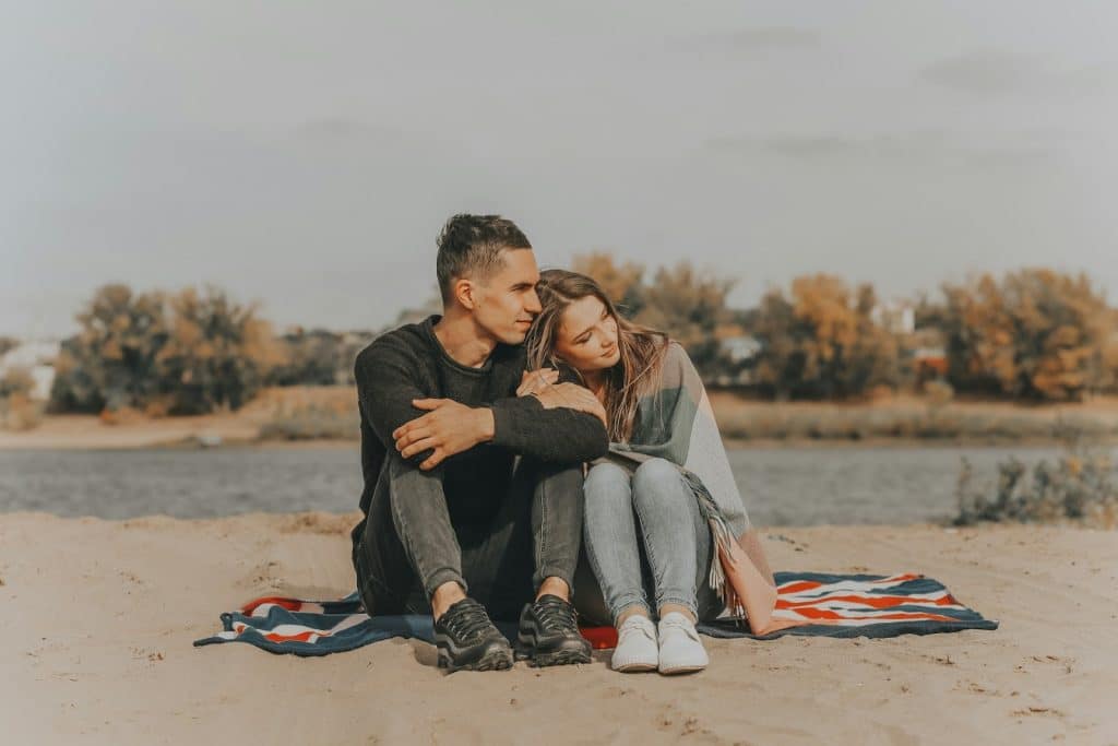 The couple is sitting on the sand.