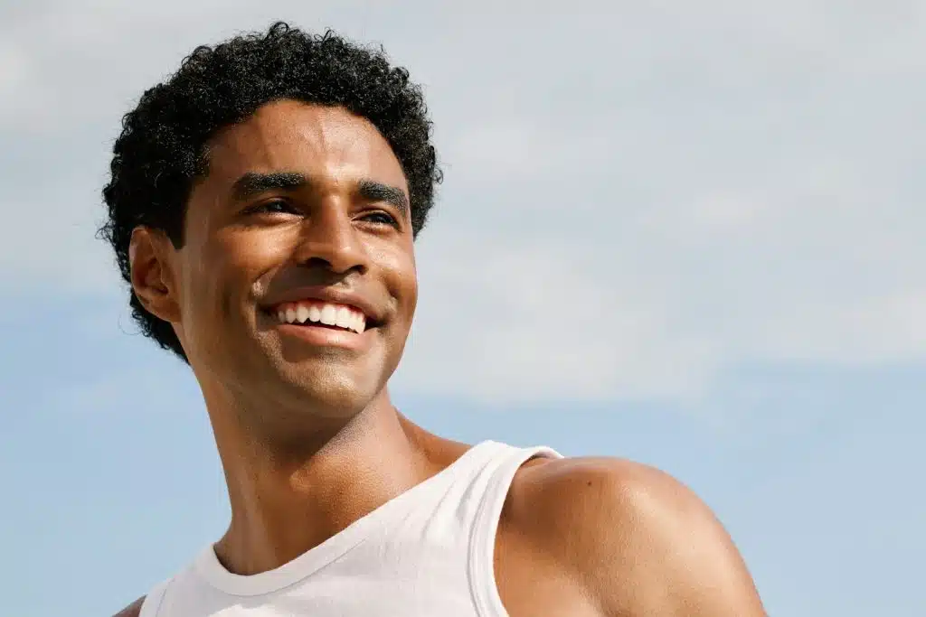 The man in a white tank top is smiling widely.