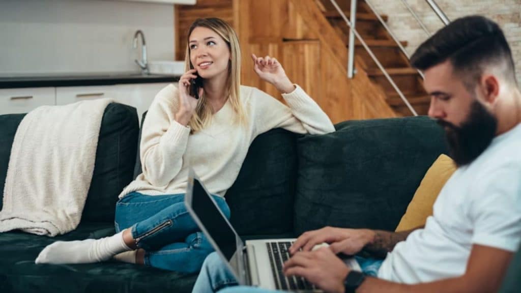 A wife laughing on the phone while her husband looks distant