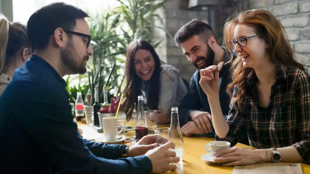 Four adults sit at a yellow table, drinking and laughing in a restaurant setting.