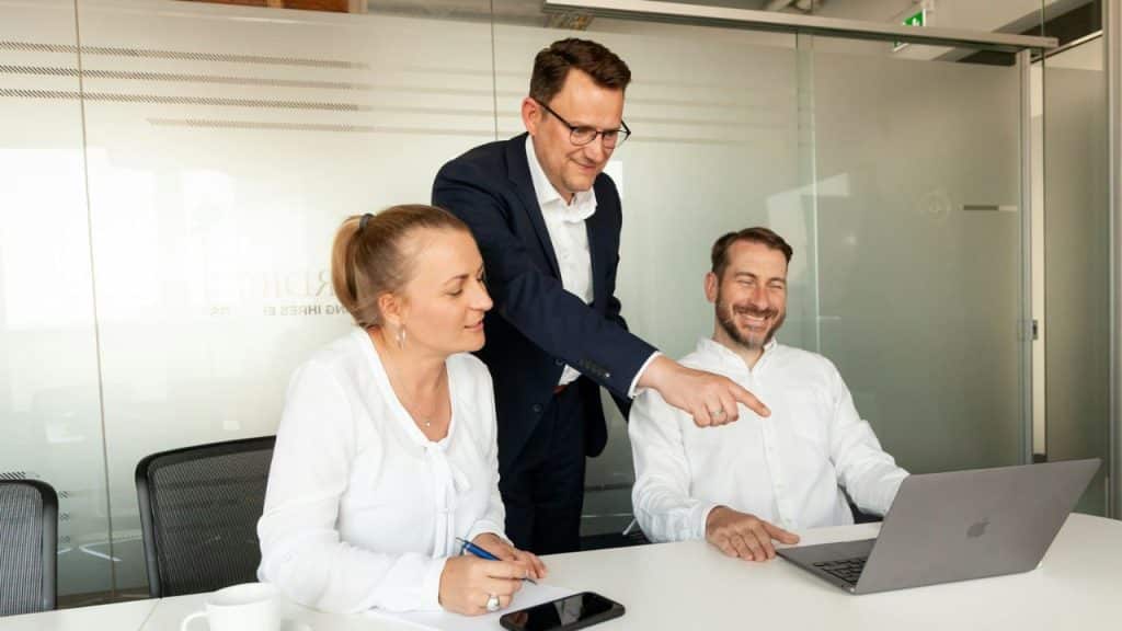 Three colleagues in an office looking at a laptop, one pointing at the screen.
