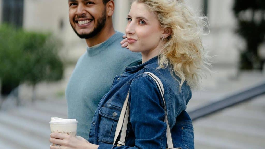 A smiling couple walking outdoors while holding a drink.
