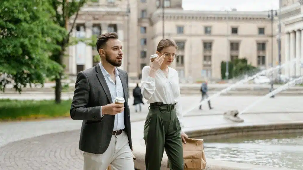 A man and woman walking near a fountain while holding coffee cups.
