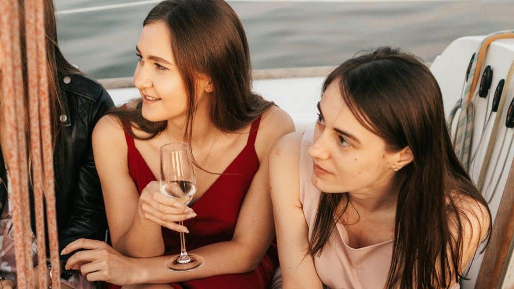 A pair of women sitting on a boat and talking while holding a wine glass.
