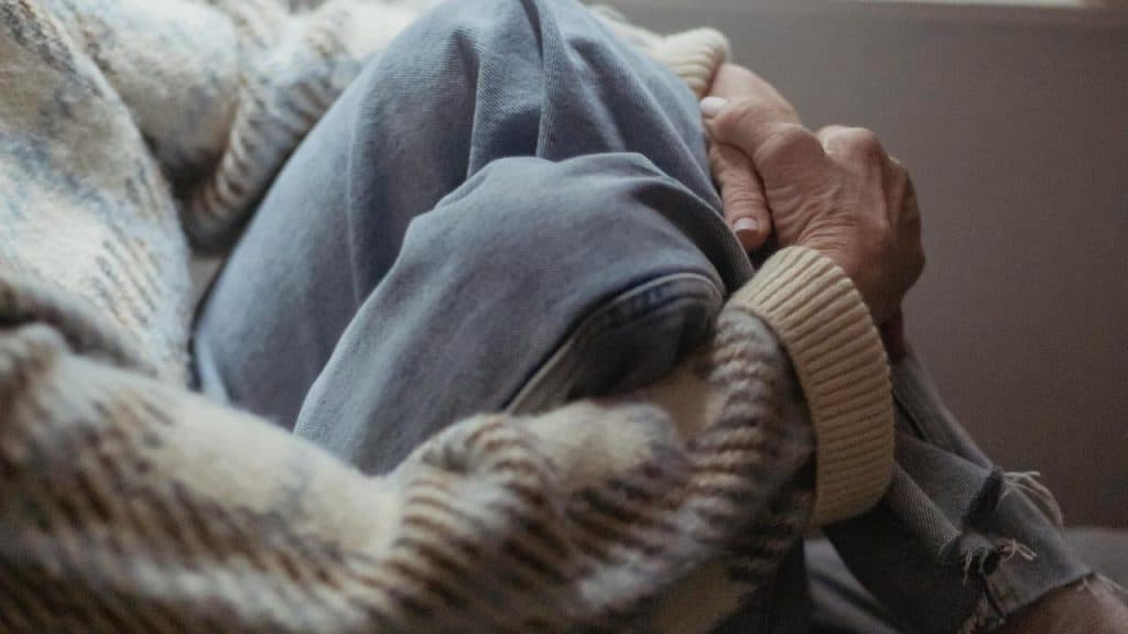 A person sitting with knees drawn up while wearing a cozy sweater and jeans.