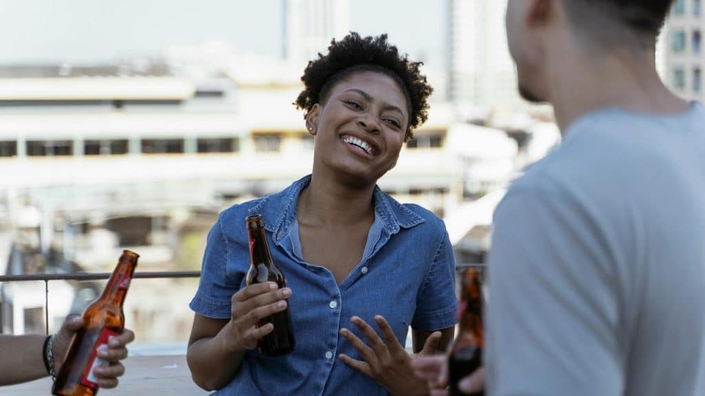 A woman laughing while holding a beer bottle during a rooftop gathering.