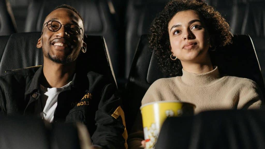 A couple sitting in a movie theater watching a film with popcorn.