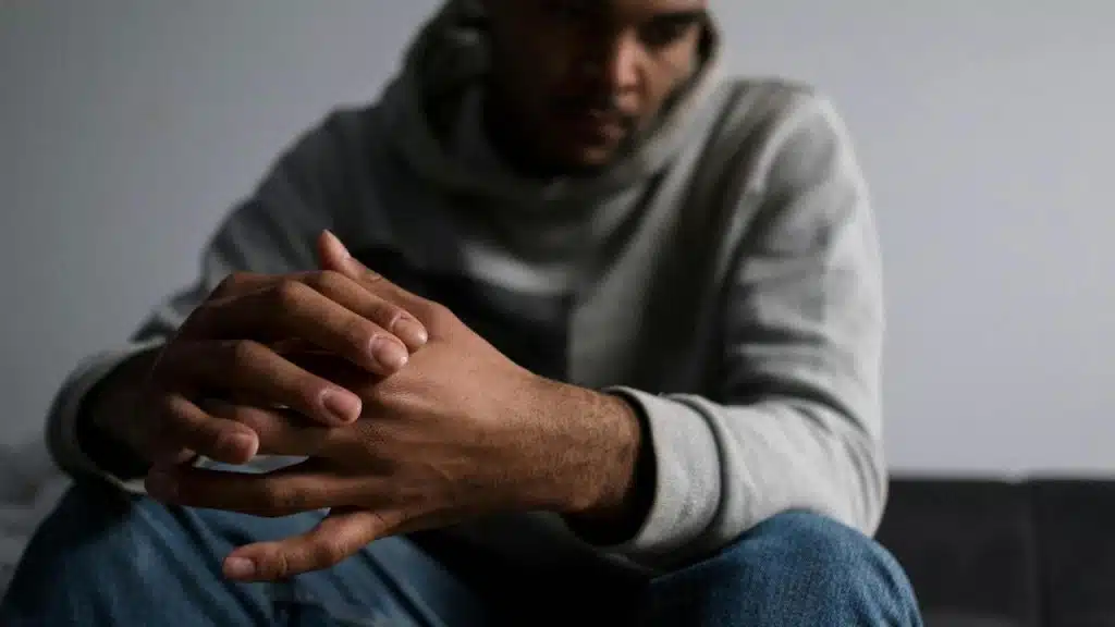 A man sitting with his hands closed together and looking down.