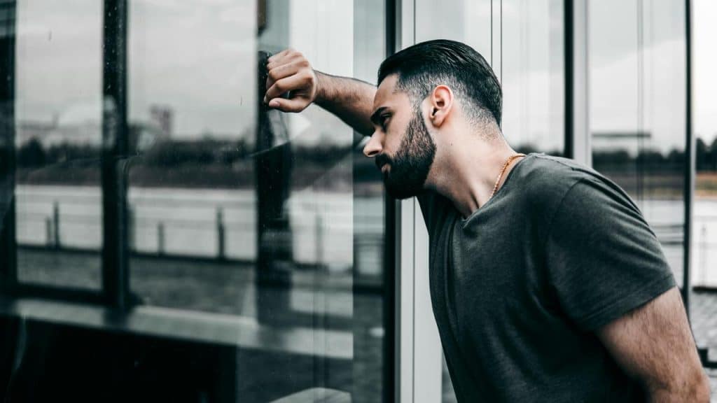 A man leaning against a glass wall with his head resting on his arm.
