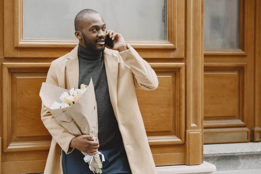 The man is calling someone on the phone while holding a bouquet.