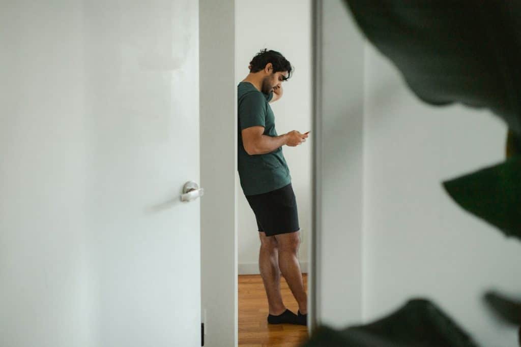 The man is standing in the doorway, looking at his phone.