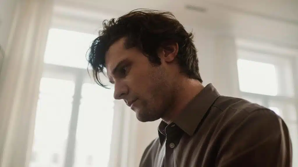 A man looking down with a serious expression indoors.