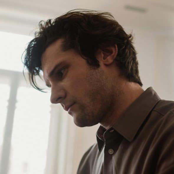 A man looking down with a serious expression indoors.