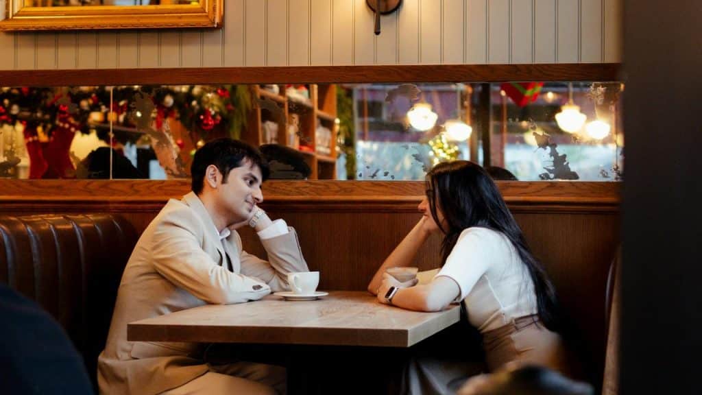 A couple sitting at a café table, smiling and talking over coffee.