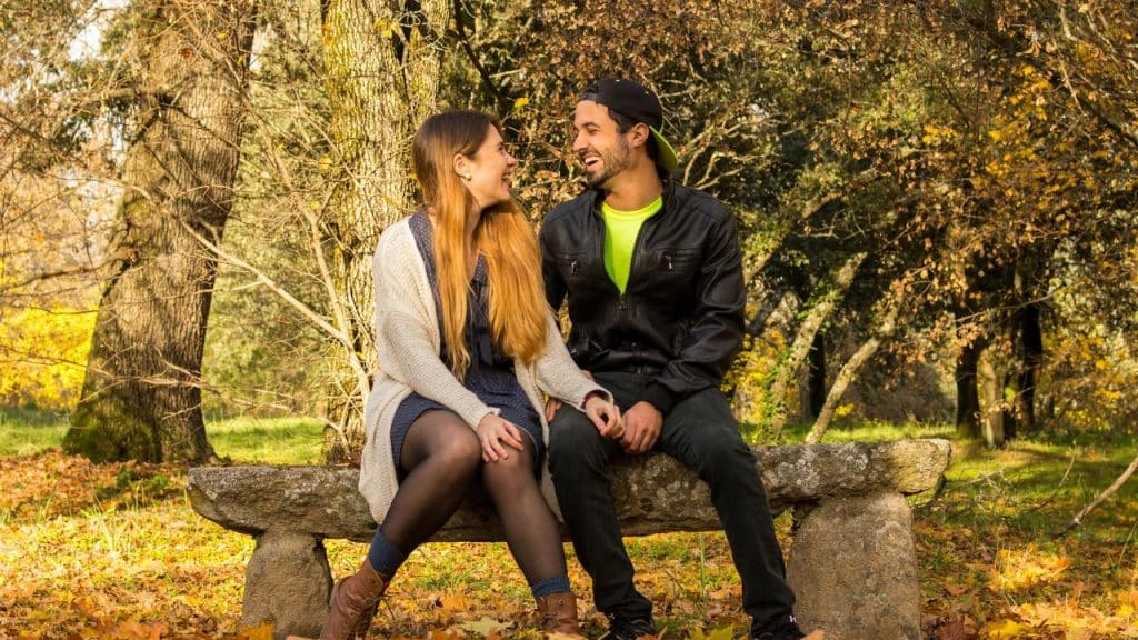 A couple sitting on a stone bench in a park, smiling and talking.