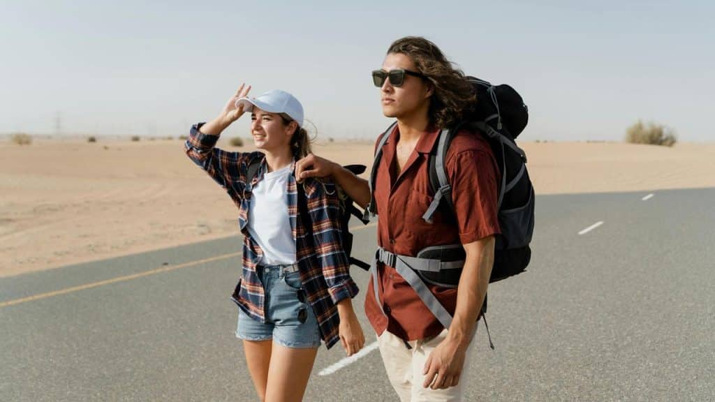 A couple walking along a desert road with backpacks, smiling and talking.