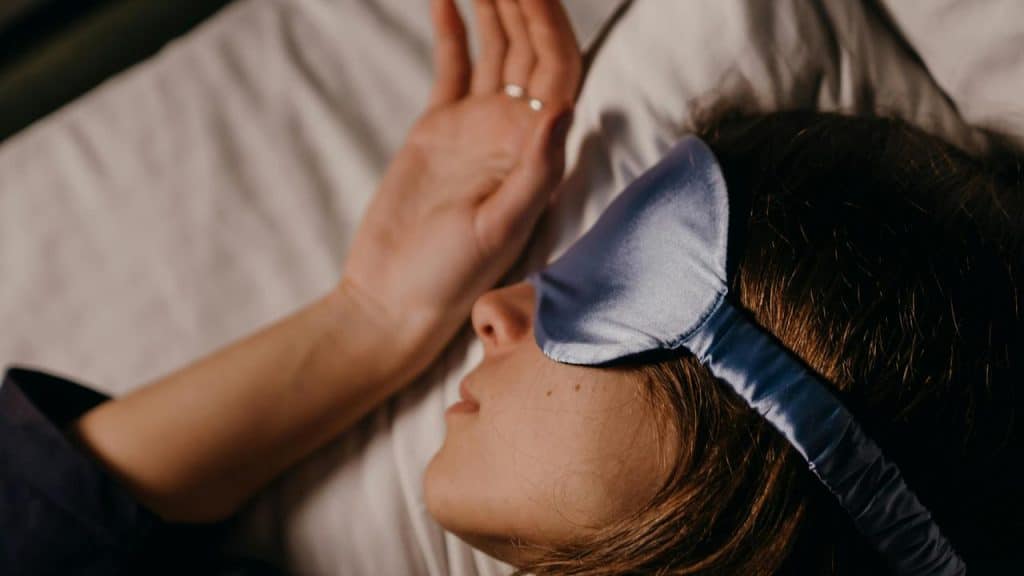 A person sleeping in bed wearing a blue sleep mask.