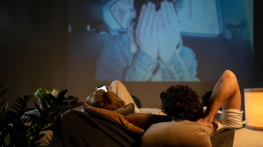 A couple lying on a bed watching a movie projected on the wall.