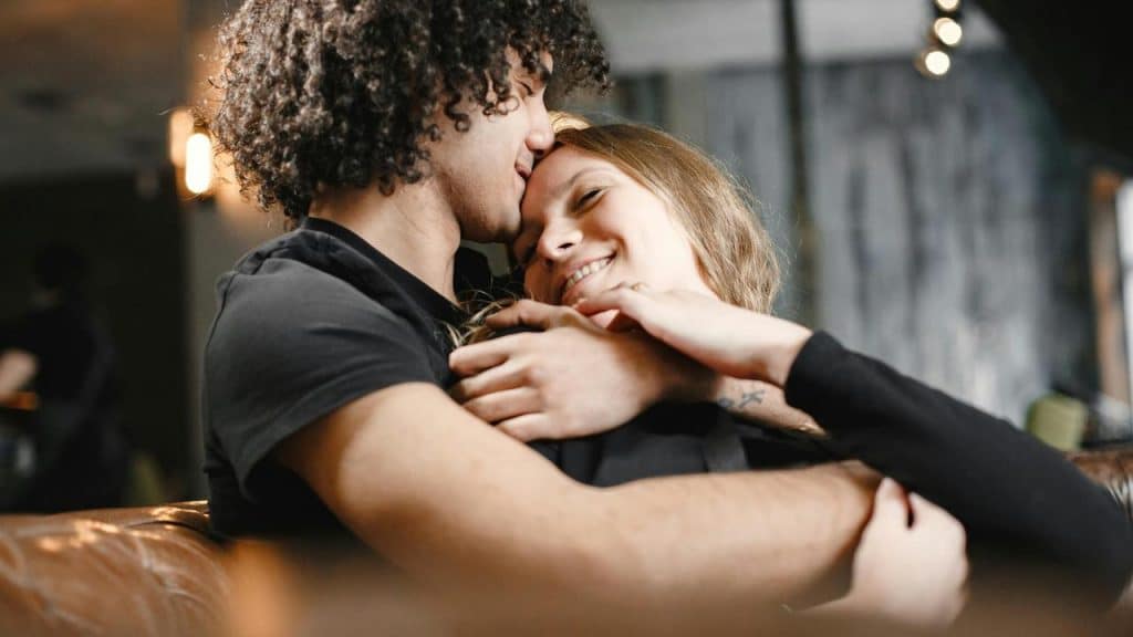 A couple cuddling on a couch and smiling at each other.