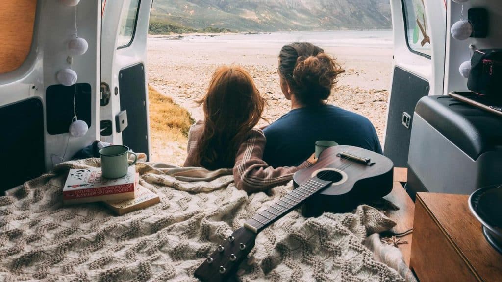 A couple relaxing in a van and looking out at the beach.
