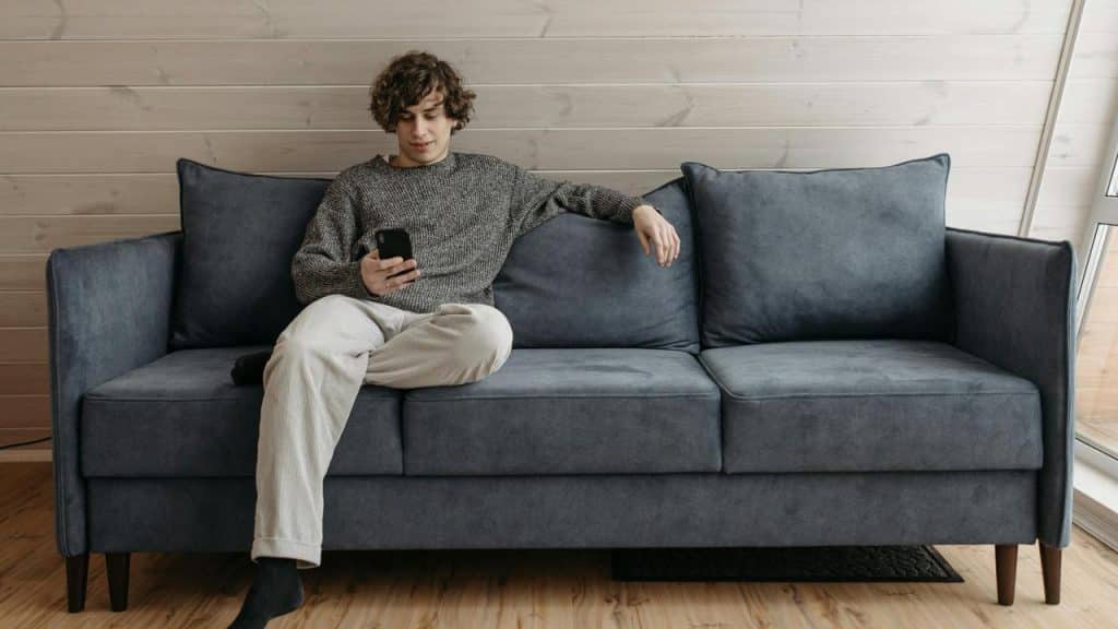 A young man sitting on a couch looking at his phone.
