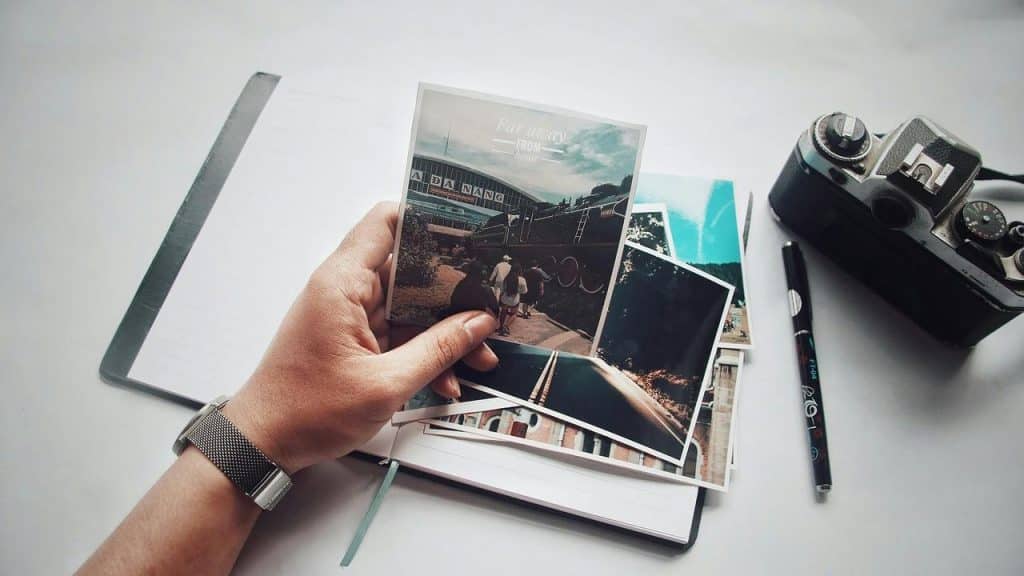 A person holding travel photos over an open notebook with a camera nearby.