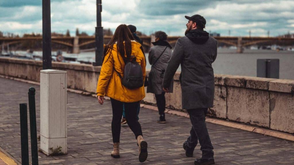 A group of people walking along a riverside path on a cloudy day.