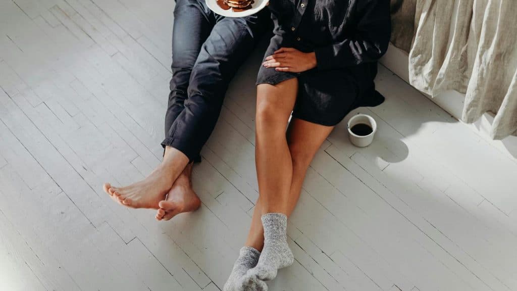 A couple sitting on the floor eating pancakes and drinking coffee.