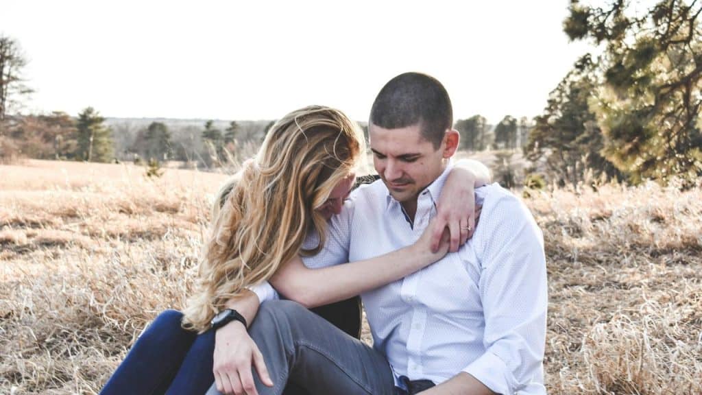 A couple sitting close together in a field, sharing a quiet moment.