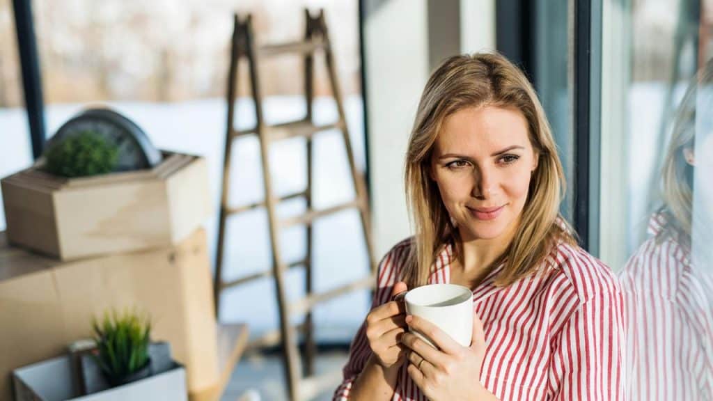 A woman holding a cup and smiling while looking out a window.