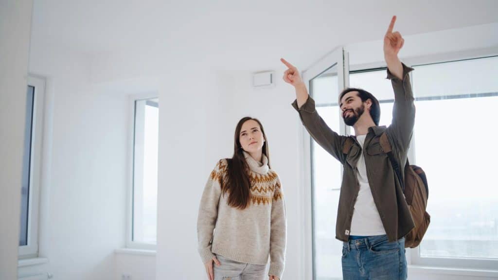 A couple standing in an empty room, discussing and pointing at the ceiling.