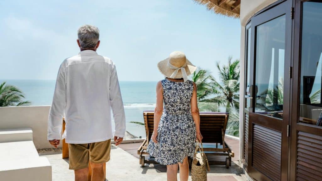 A mature couple walking toward a beach with lounge chairs and an ocean view.