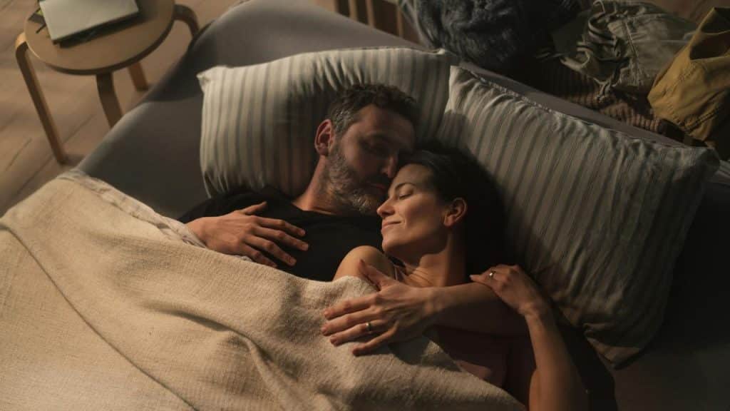 A couple cuddling in bed with peaceful expressions.
