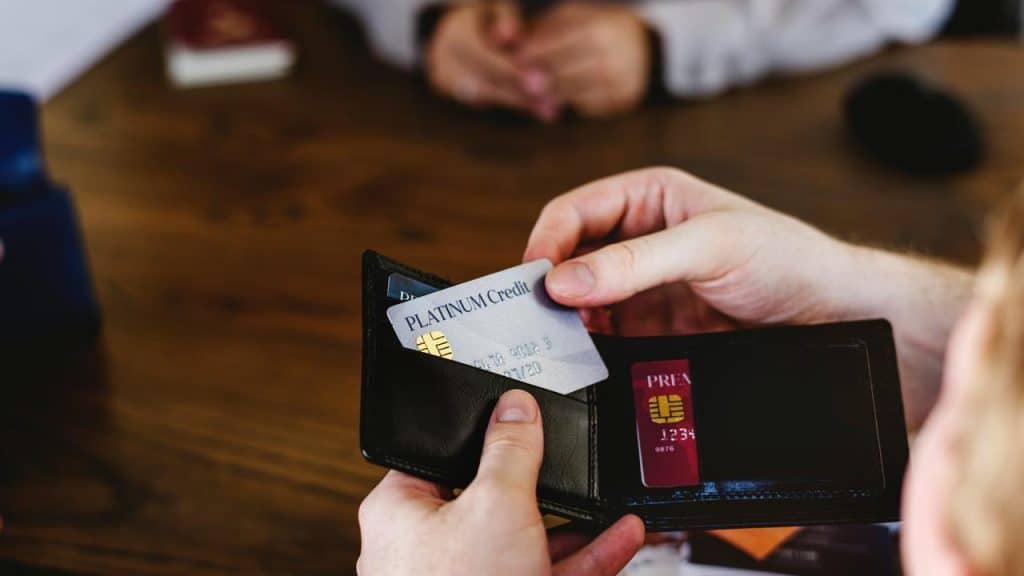 A person holding a wallet with multiple credit cards at a table.