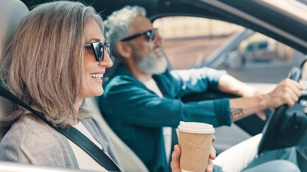 A mature couple smiling while driving with coffee in hand.